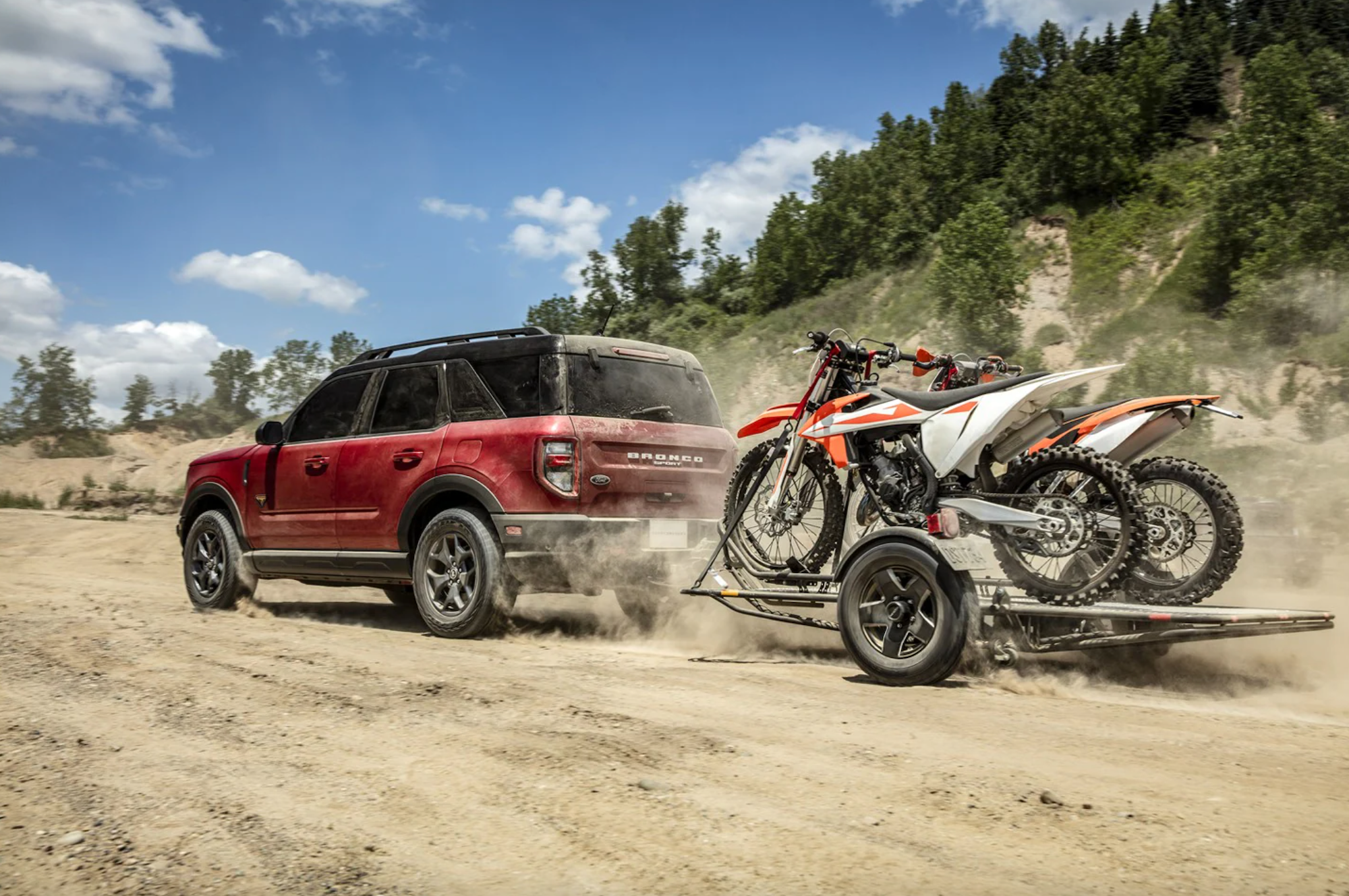 A dark-red 2021 Ford Bronco Sport SUV towing two dirt bikes on a dusty trail