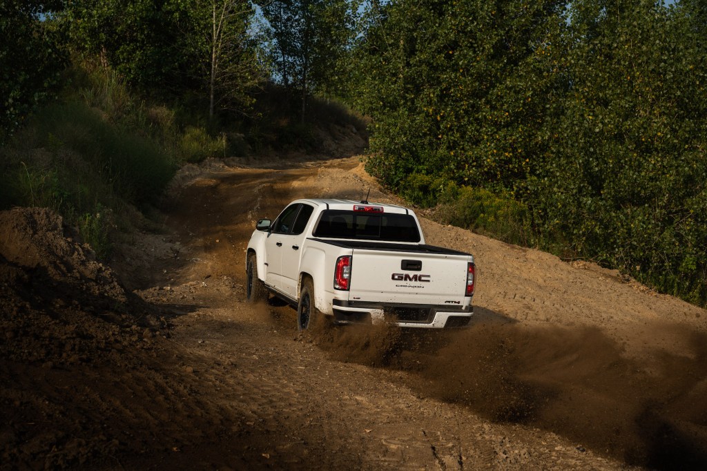 A white 2021 GMC Canyon AT4 Off-Road Performance Edition midsize pickup kicks up dirt as it travels up a hill
