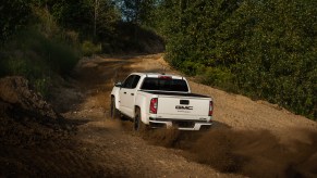 A white 2021 GMC Canyon AT4 Off-Road Performance Edition midsize pickup kicks up dirt as it travels up a hill
