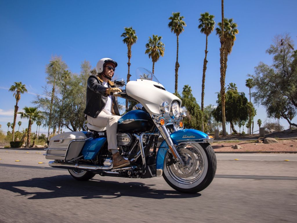 A rider takes a blue-and-white 2021 Harley-Davidson Electra Glide Revival down a palm-tree-lined street