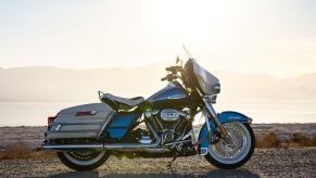 The side view of a blue-and-white 2021 Harley-Davidson Electra Glide Revival on a rocky beach