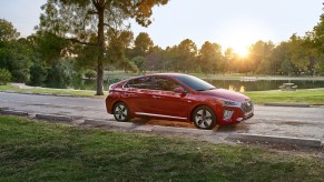 A red 2021 Ioniq Hybrid sedan parked on a road overlooking a lake and trees as the sun hangs low in the sky