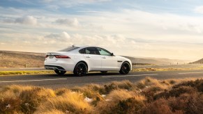 A white 2021 Jaguar XF luxury sedan stopped on a two-lane highway through arid plains