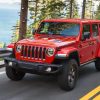 A red 2021 Jeep Wrangler Rubicon Unlimited drives on a forest road overlooking a lake