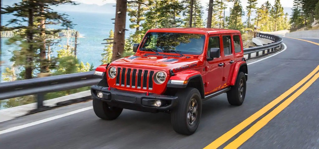 A red 2021 Jeep Wrangler Rubicon Unlimited drives on a forest road overlooking a lake