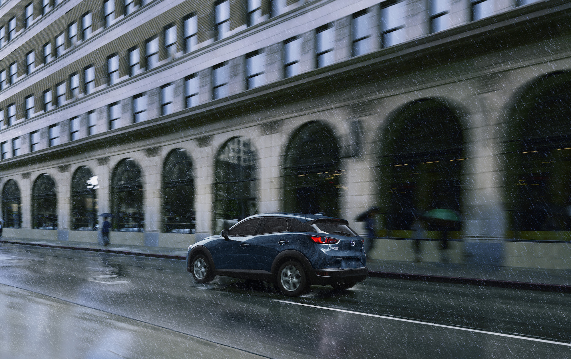 A blue 2021 Mazda CX-3 Sport subcompact SUV drives on a city street in the rain