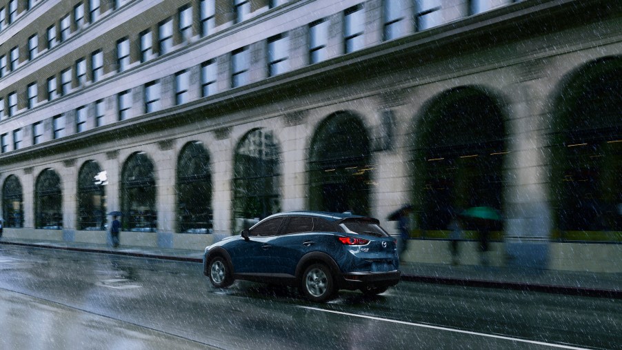 A blue 2021 Mazda CX-3 Sport subcompact SUV drives on a city street in the rain