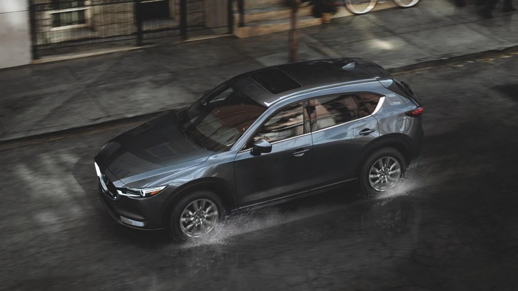 A dark colored Mazda CX-5 splashes through a puddle in the city. 