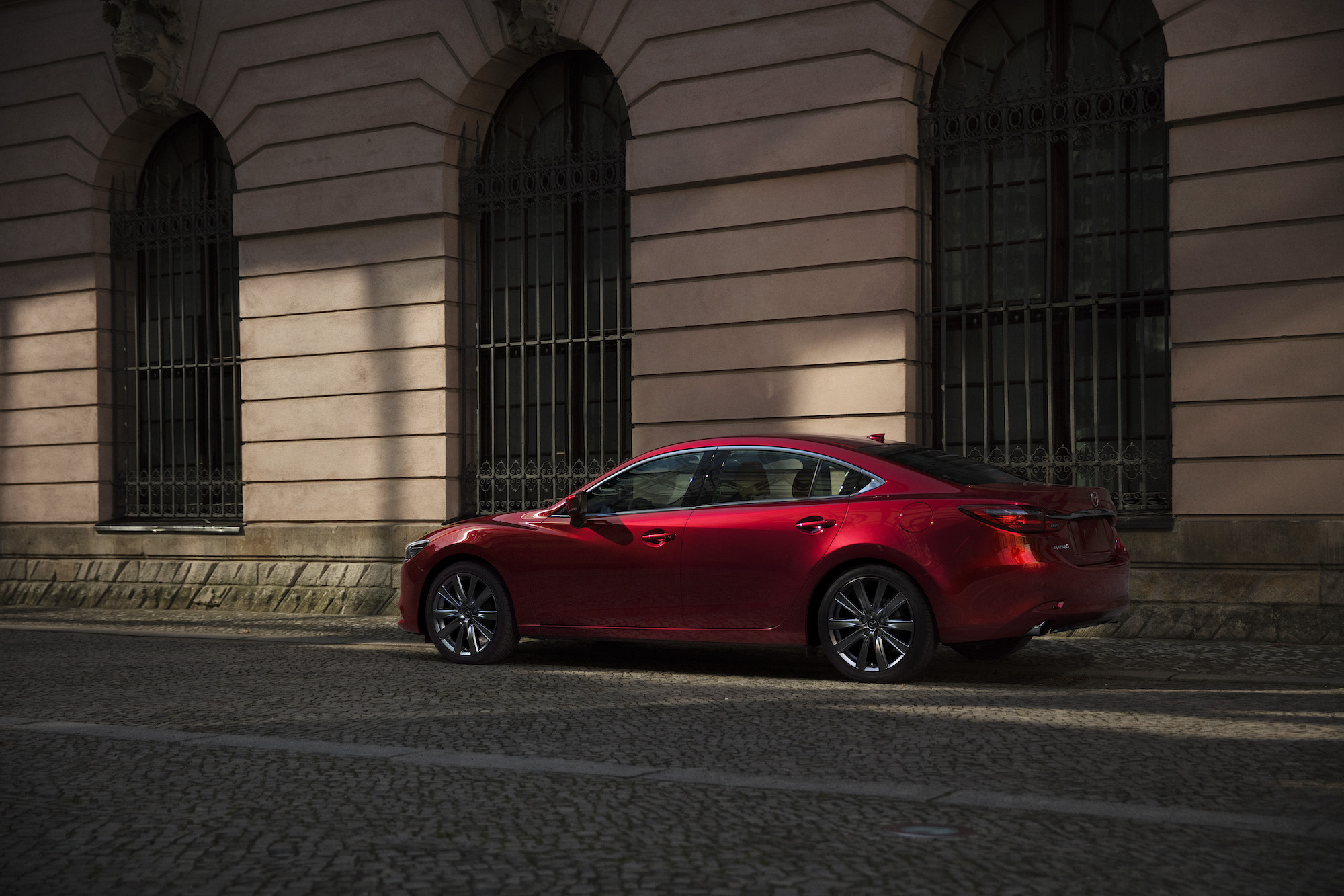 A red 2021 Mazda6 midsize sedan parked along a curb outside a city building