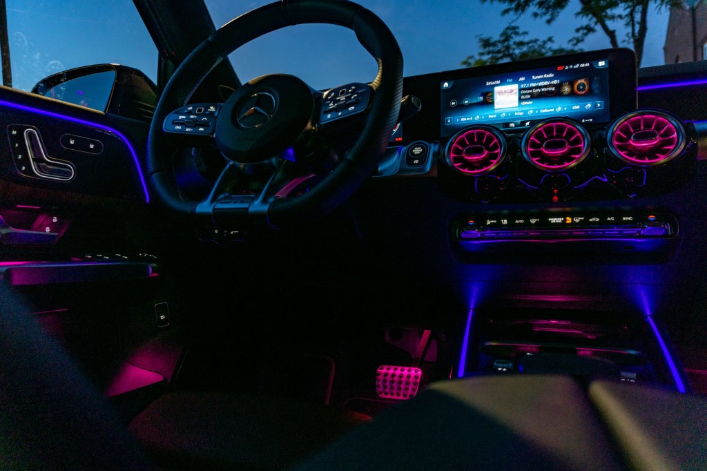 The driver's side front interior of a 2021 Mercedes-AMG GLB 35 with its ambient lighting turned on at night