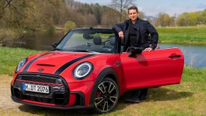A man standing next to a red 2021 Mini Cooper John Cooper Works convertible parked in the grass beside a river