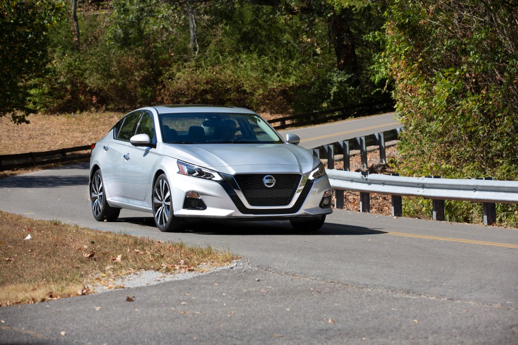 A silver 2021 Nissan Altima midsize sedan traveling on a curvy two-lane highway through trees