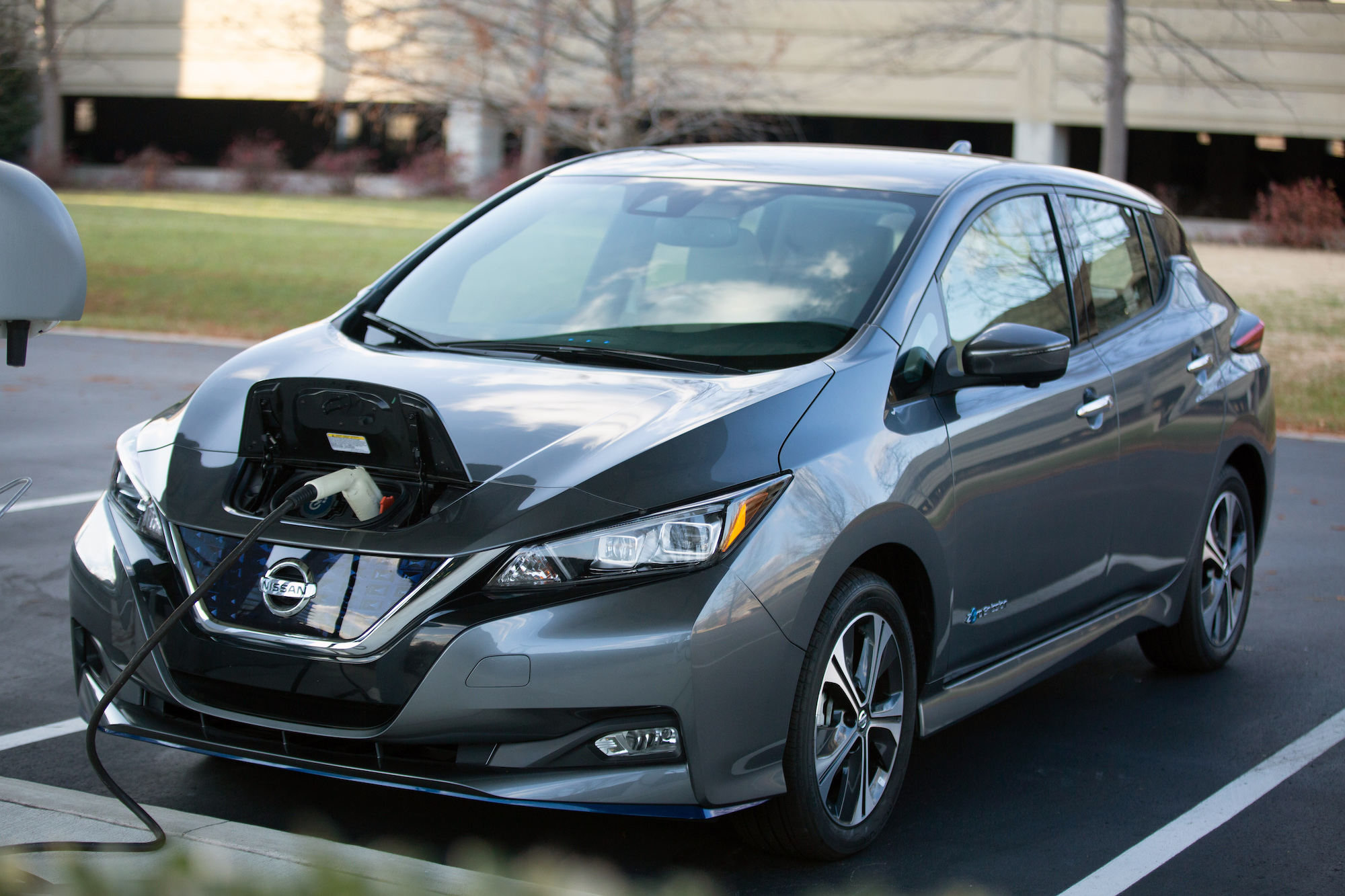 A dark-gray metallic 2021 Nissan Leaf in a parking space at a charging station