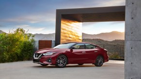 A red 2021 Nissan Maxima sedan parked outside a modern concrete home overlooking mountains