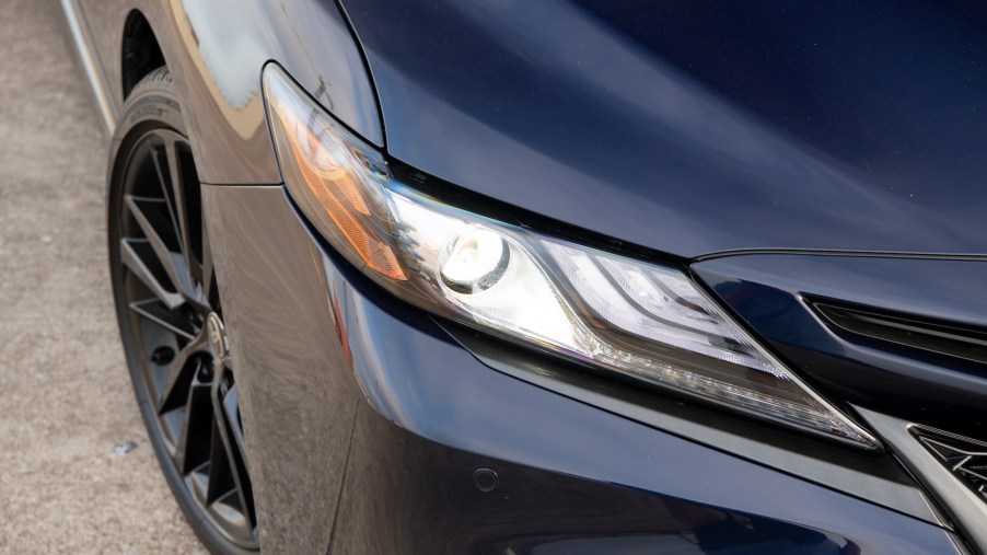 Closeup view of a dark-blue 2021 Toyota Camry XSE sedan's passenger-side hood, headlight, front bumper, and tire