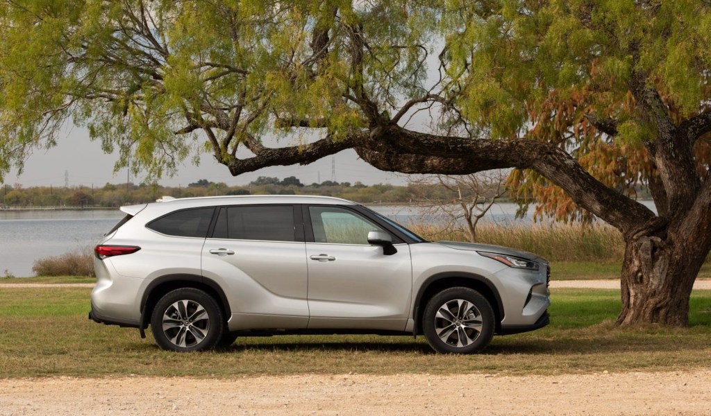 A silver 2021 Toyota Highlander XLE midsize SUV parked under a tree overlooking a body of water