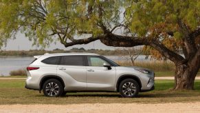 A silver 2021 Toyota Highlander XLE midsize SUV parked under a tree overlooking a body of water