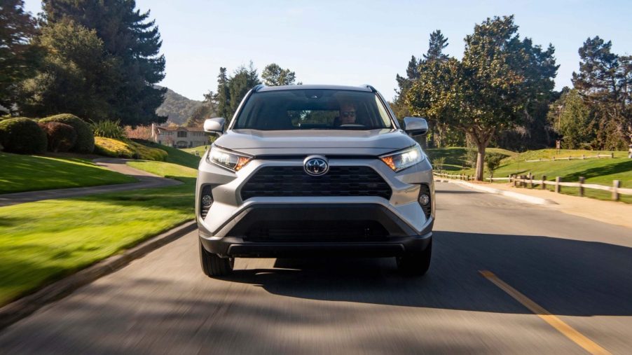 A front view of a silver 2021 Toyota RAV4 XLE FWD traveling on a suburban street past green grass and trees