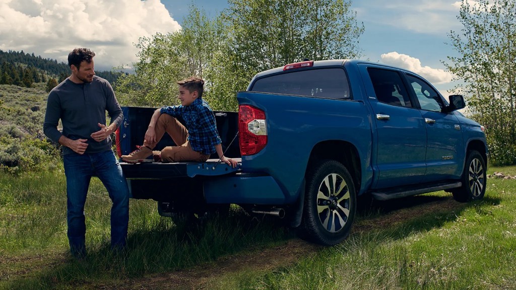 A father talks to his son who is sitting in the bed of a blue 2021 Toyota Tundra. 