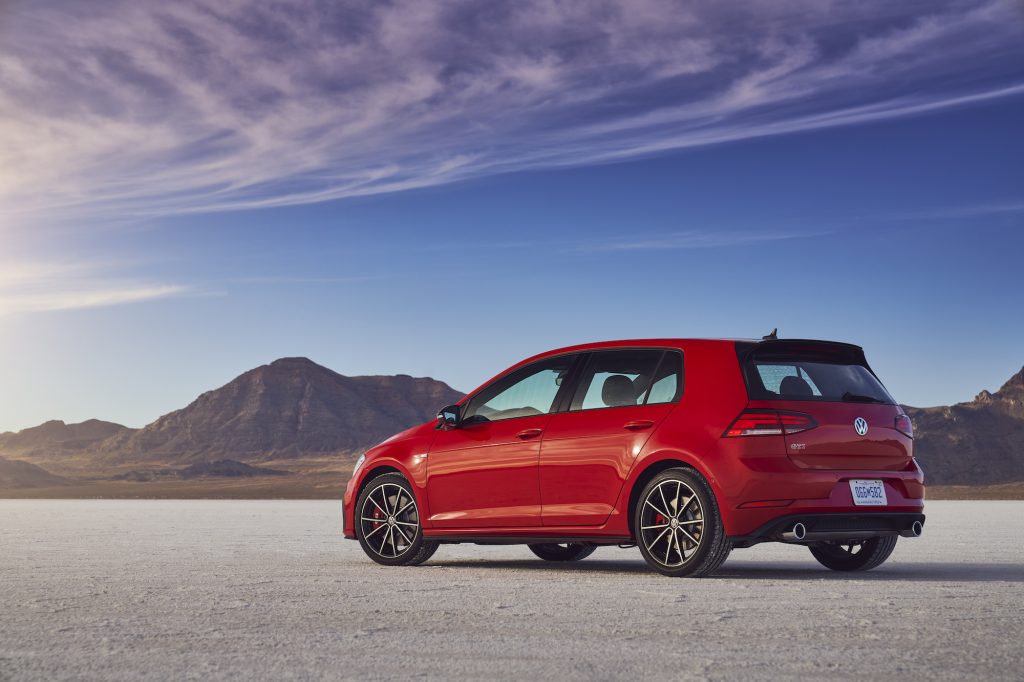 A red 2021 Volkswagen Golf GTI hatchback parked in a desert with mountains and blue sky