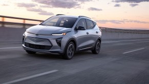 A silver 2022 Chevrolet Bolt EUV electric crossover traveling on a highway as the sun sits low in a mostly clear sky