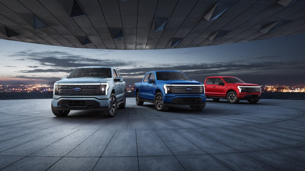 2022 Ford F-150 Lightning Platinum, Lariat, and XLT pre-production models overlooking a city skyline at night