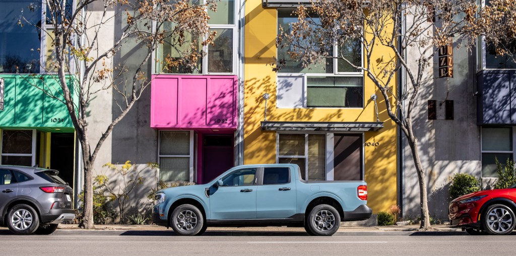 A powder-blue 2022 Ford Maverick Hybrid XLT pickup truck paked on a city street outside a colorful building