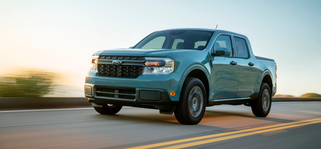 A powder-blue 2022 Ford Maverick Hybrid XLT compact pickup truck travels on a two-lane highway