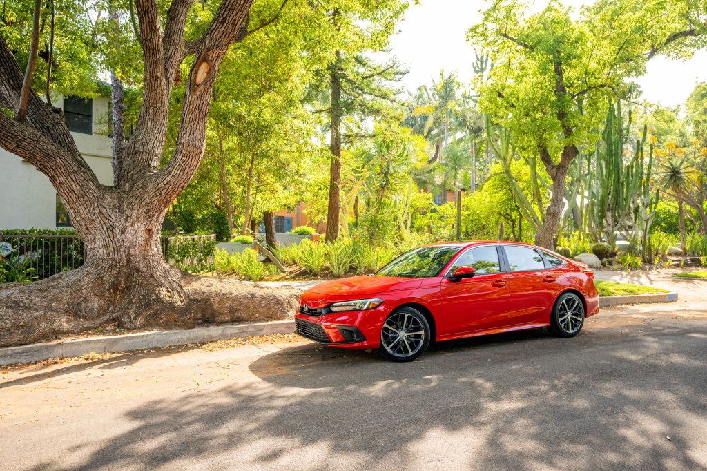The side 3/4 view of a red 2022 Honda Civic Sedan Touring parked on a tree-lined street by a house