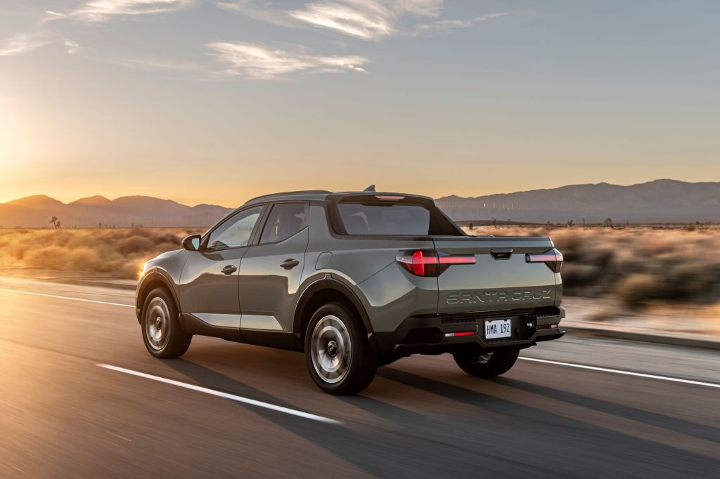The rear 3/4 view of a gray-green 2022 Hyundai Santa Cruz driving down a desert road