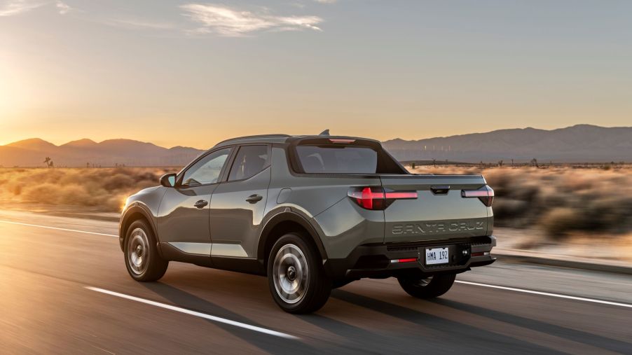 The rear 3/4 view of a gray-green 2022 Hyundai Santa Cruz driving down a desert road