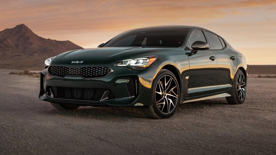 A dark colored 2022 Kia Stinger sits on a dirt road with a small hill behind it.