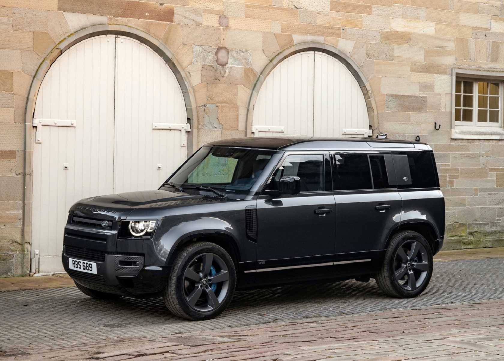 A black 2022 Land Rover Defender V8 parked by a tan stone building