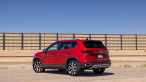 A red 2022 Volkswagen Taos SE 4Motion subcompact crossover SUV parked on asphalt next to a fence under a clear blue sky