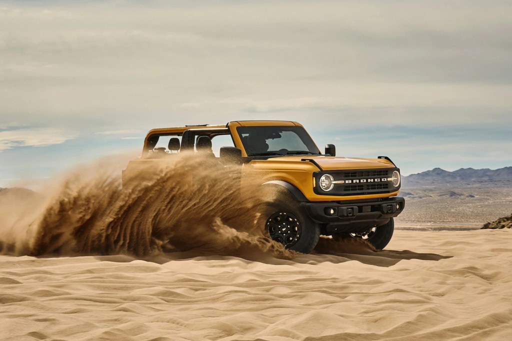 The yellow Ford Bronco plays sideways in the sand