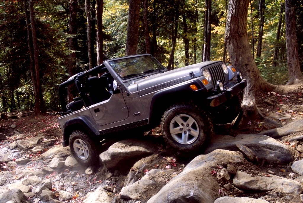 A silver Jeep Wrangler clambers up rocks on a trail