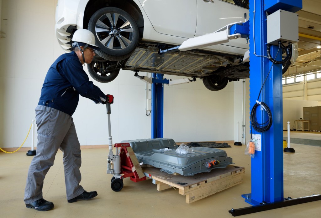 A blue-clothed 4R Energy employee moves a used battery pack from a white Nissan Leaf at a recycling facility
