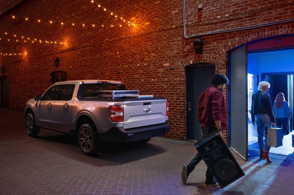 A 2022 Ford Maverick compact pickup truck parked outside of a live music venue in an urban area