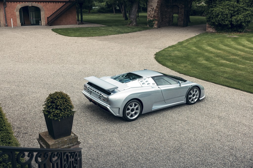 An overhead rear 3/4 view of a silver Bugatti EB110 SS on the grounds of a chateau
