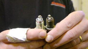 A black-shirted mechanic compares old and new spark plugs while changing them