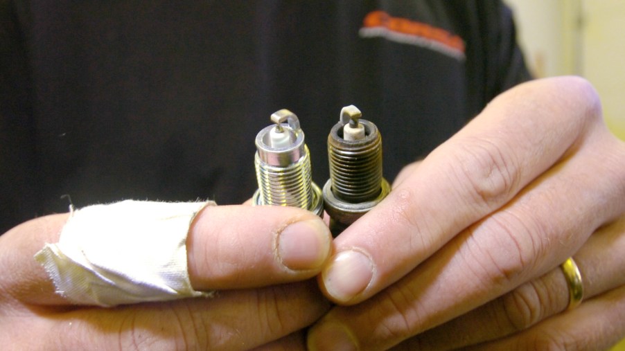 A black-shirted mechanic compares old and new spark plugs while changing them
