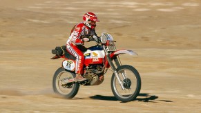 Red-clad Cyril Neveu on the red-and-white 1982 Honda XR500R Dakar Rally bike racing through the desert