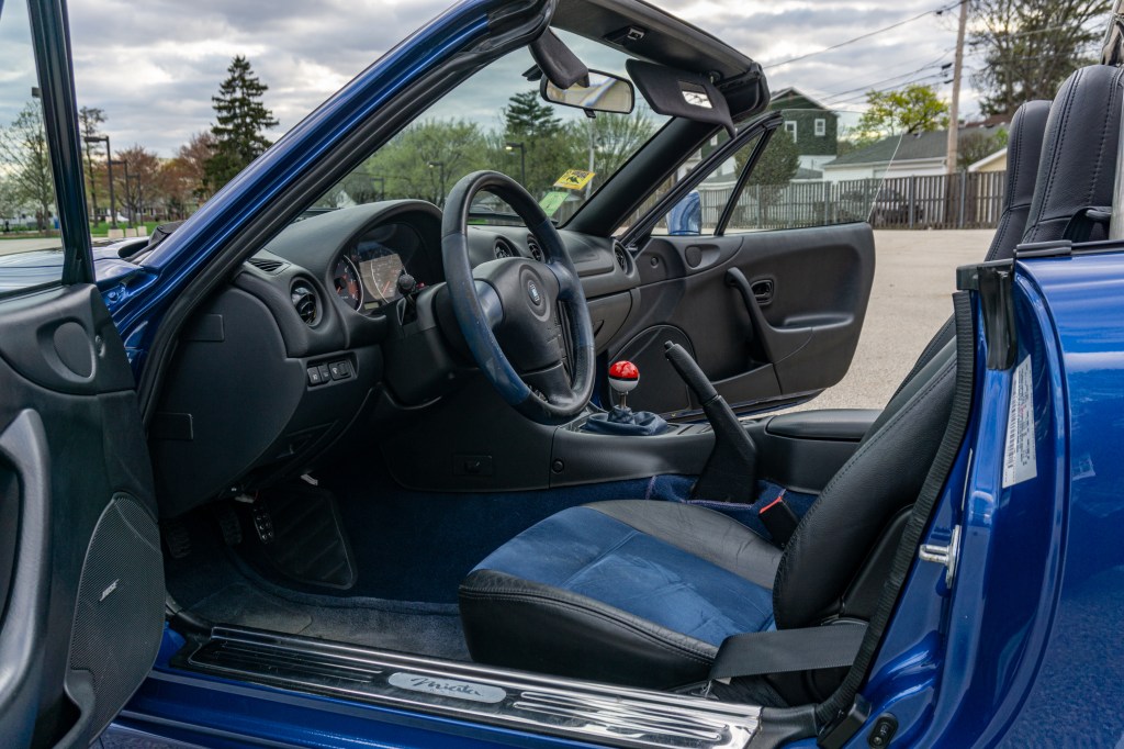 The blue-and-black interior of a blue 1999 Mazda MX-5 Miata 10th Anniversary Edition with its roof down