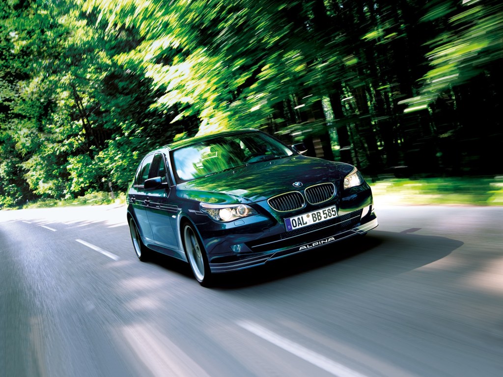 A black E60 BMW Alpina B5 S drives down a forest-lined road