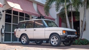 The white ECD Automotive Design electric Range Rover Classic plugged into a charger by a white building