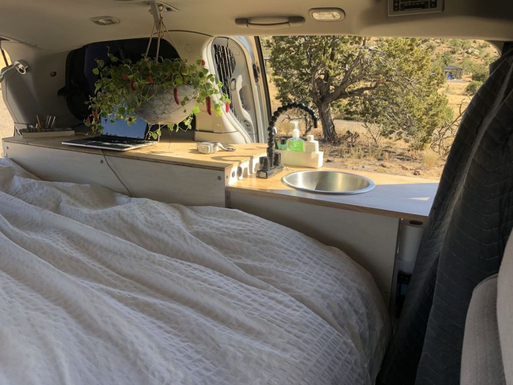 Nissan Quest camper interior with the bed made and a scenic view 