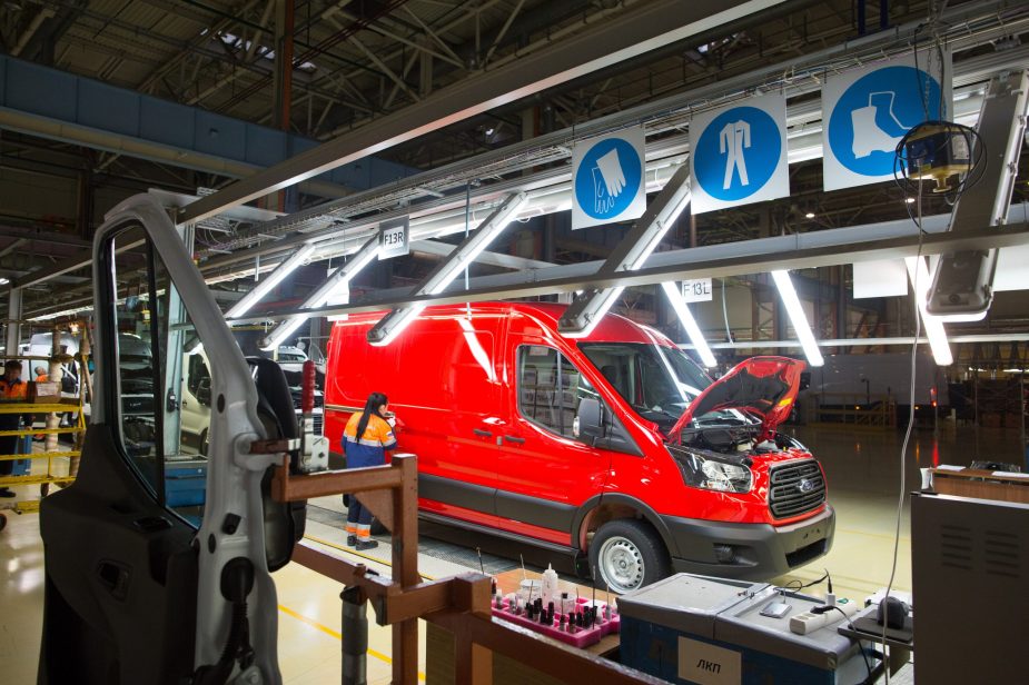 A worker performs a quality control check on a red Ford Transit van inside a light tunnel at the Ford Sollers production plant in Elabuga, Russia