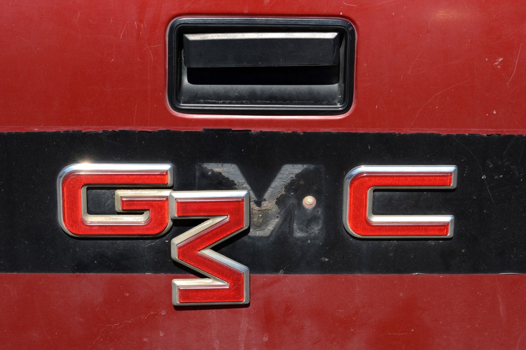 An aged red GMC pickup truck tailgate with a dangling logo