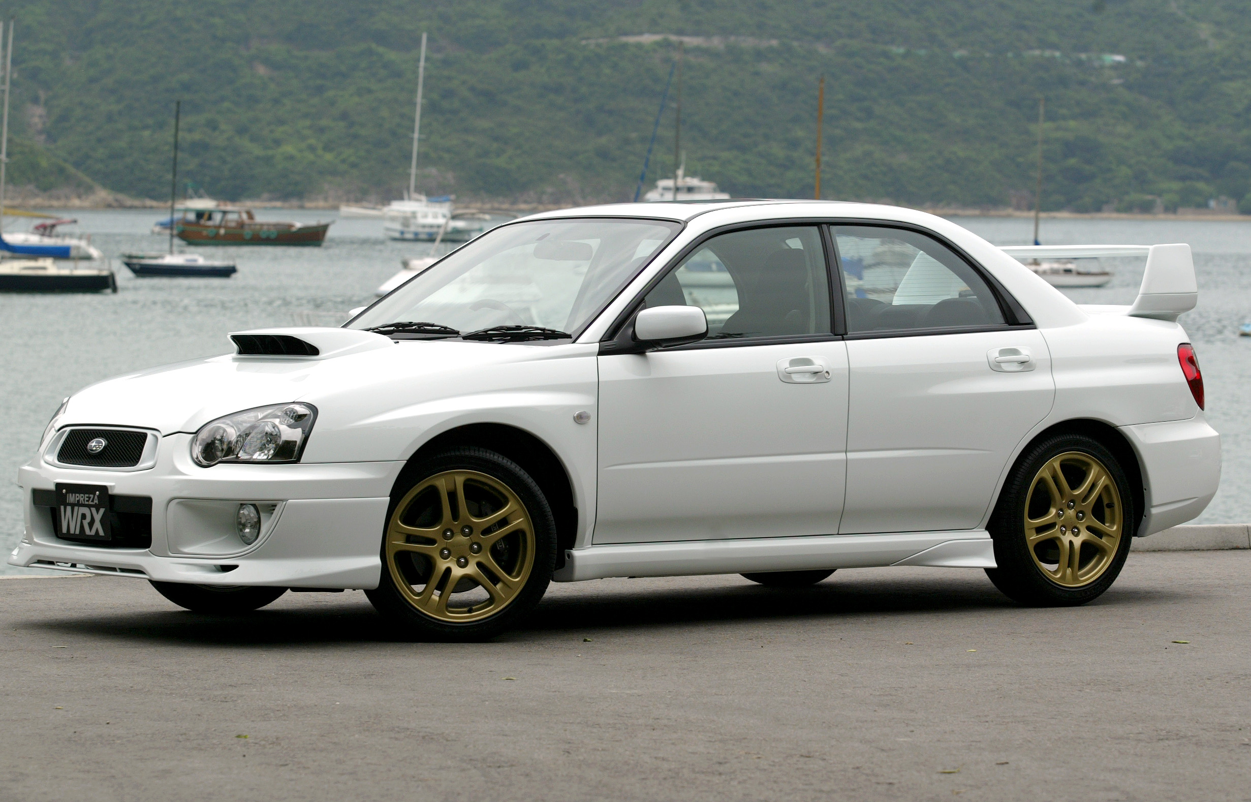 A white Subaru WRX with gold wheels and spoiler