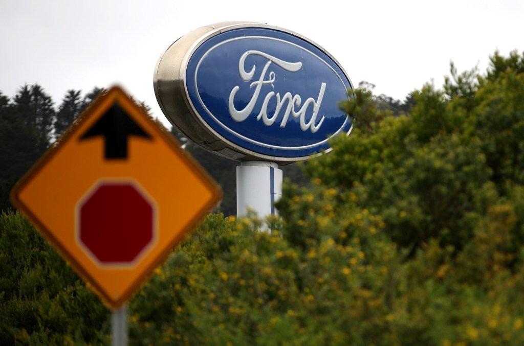 A gigantic Ford dealership sign with a stop sign in the foreground